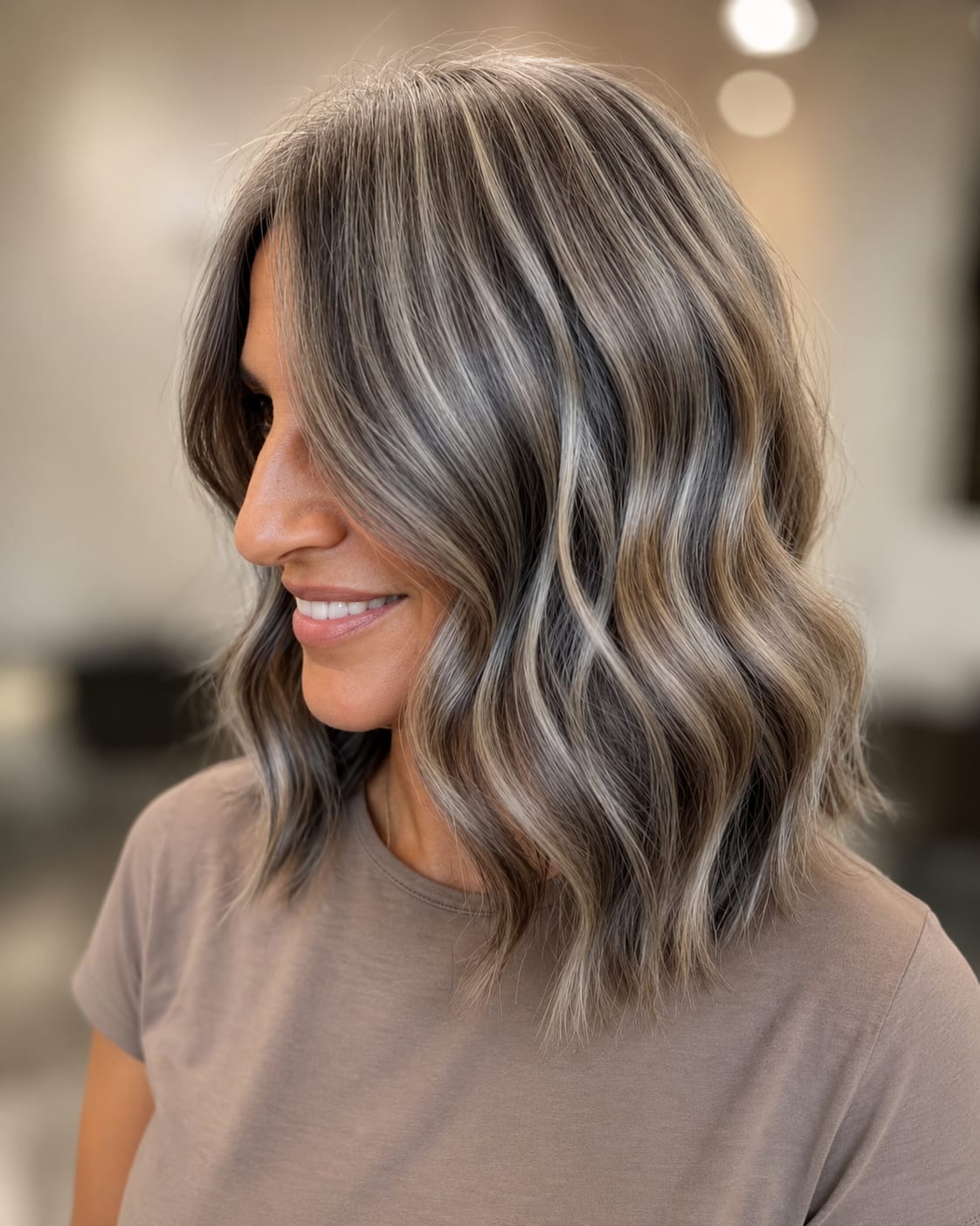 A client smiling, with a wavy lob softly blended from warm brown through to silver