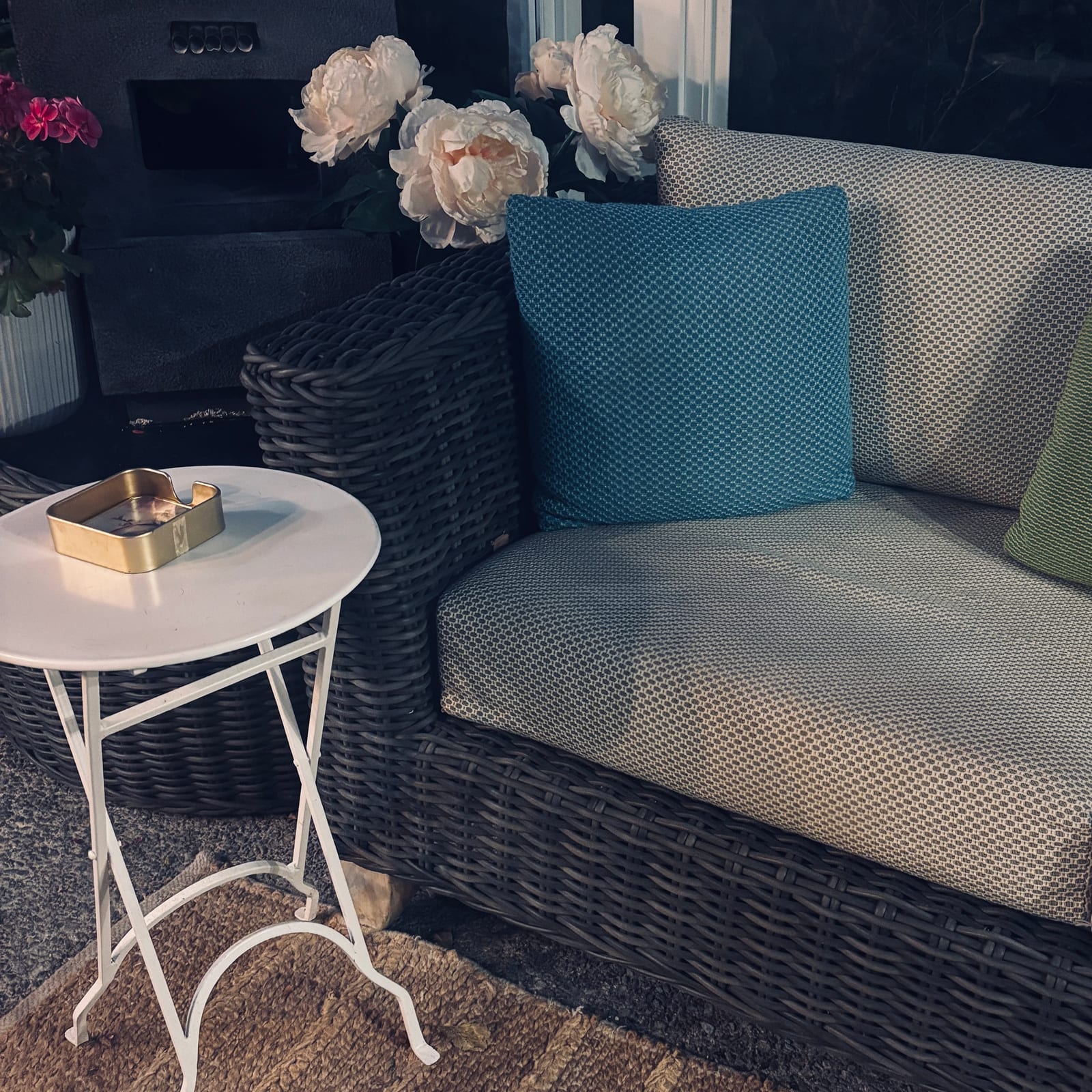 A quiet seating corner inside the studio — woven sofa, peonies, a small table